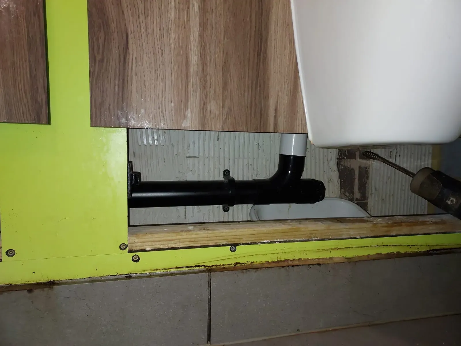 A plumber's snake tool being used to clear a blocked drain pipe under a sink or toilet.