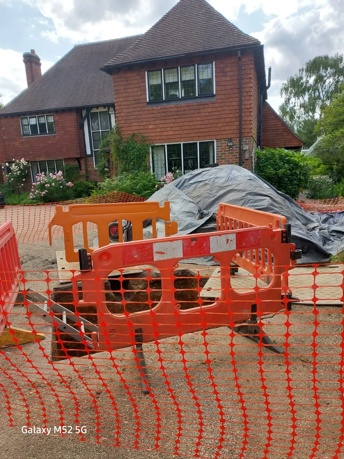 Drainage excavation work with safety barriers in front of a house, indicating drain repairs or new installations.