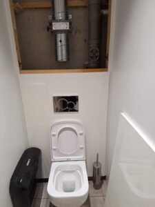 Access panel removed from behind toilet to access pipework